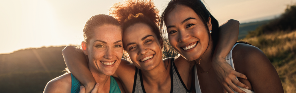 Three women smiling and hugging outside on hills just before sunset