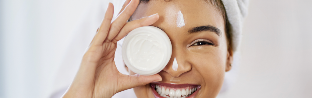 Woman smiling and holding skin cream over one eye like a monocle